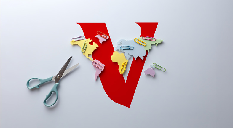 Large red letter V with colourful paper cut-outs of world map regions attached by paper clips, alongside a pair of scissors, representing connected global markets or international investment.